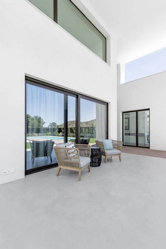 Light-coloured courtyard flooring and seating in front of glass doors